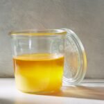 A glass jar filled with a golden yellow liquid, with a glass lid leaning against it.
