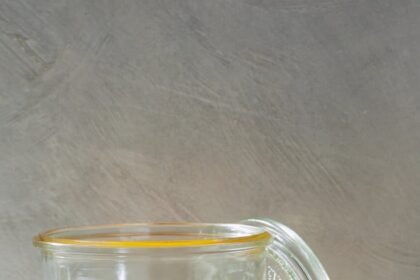 A glass jar filled with a golden yellow liquid, with a glass lid leaning against it.