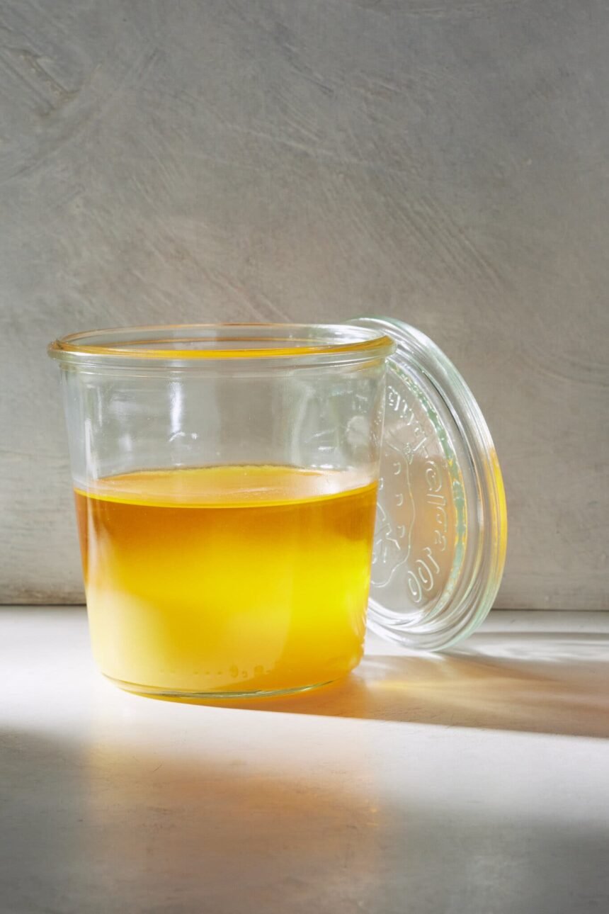 A glass jar filled with a golden yellow liquid, with a glass lid leaning against it.
