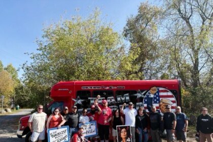 A group of people, with protest signs, standing in front of a red bus that reads "SAVING THE MOTDERF**KING WORLD!" and "MAGABUS."