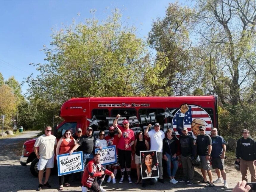 A group of people, with protest signs, standing in front of a red bus that reads "SAVING THE MOTDERF**KING WORLD!" and "MAGABUS."